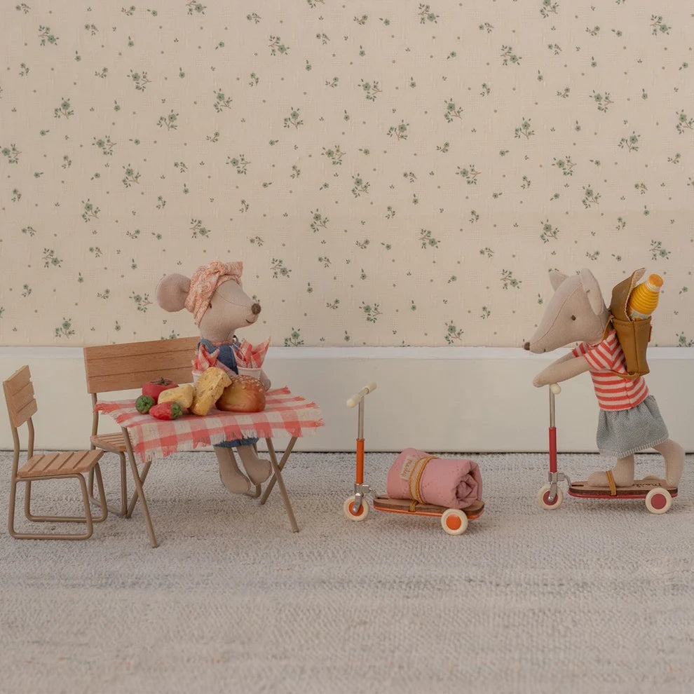 Two toy mice with a table and chairs, one on a scooter, against a floral wallpaper background.